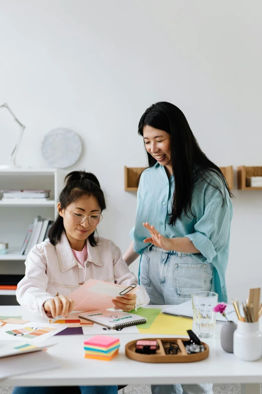 a woman and a little girl sitting at a table, by Jang Seung-eop, trending on pexels, academic art, standing on a desk, designer product, holding notebook, inspect in inventory image