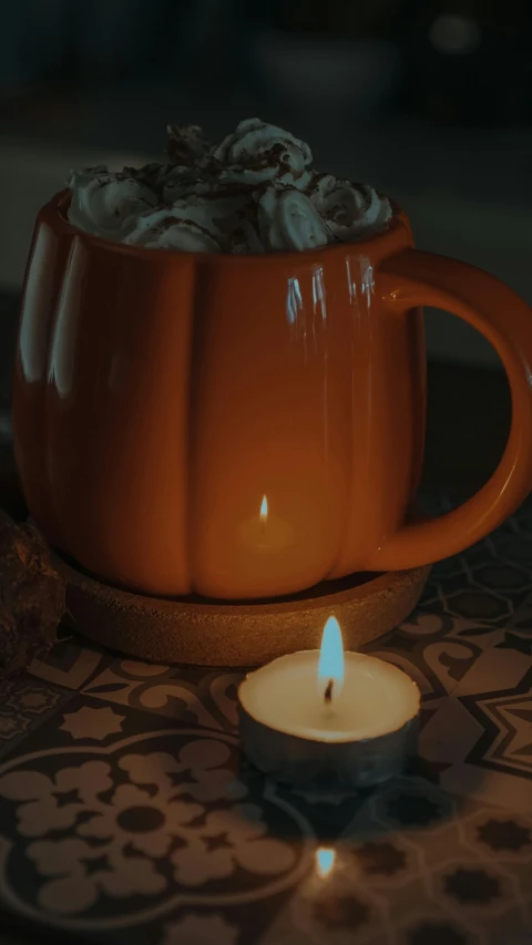 a cup of hot chocolate next to a lit candle, inspired by Elsa Bleda, pexels, hurufiyya, jack - o'- lantern, mid view, square, pumpkin