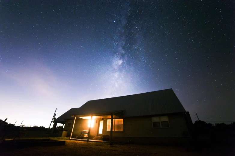 a house at night with the milky in the background, by Robert Childress, unsplash contest winner, light and space, oklahoma, very wide angle view, bright sky, cottage