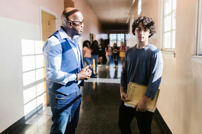 two men standing next to each other in a hallway, teacher, black teenage boy, on set, gen z