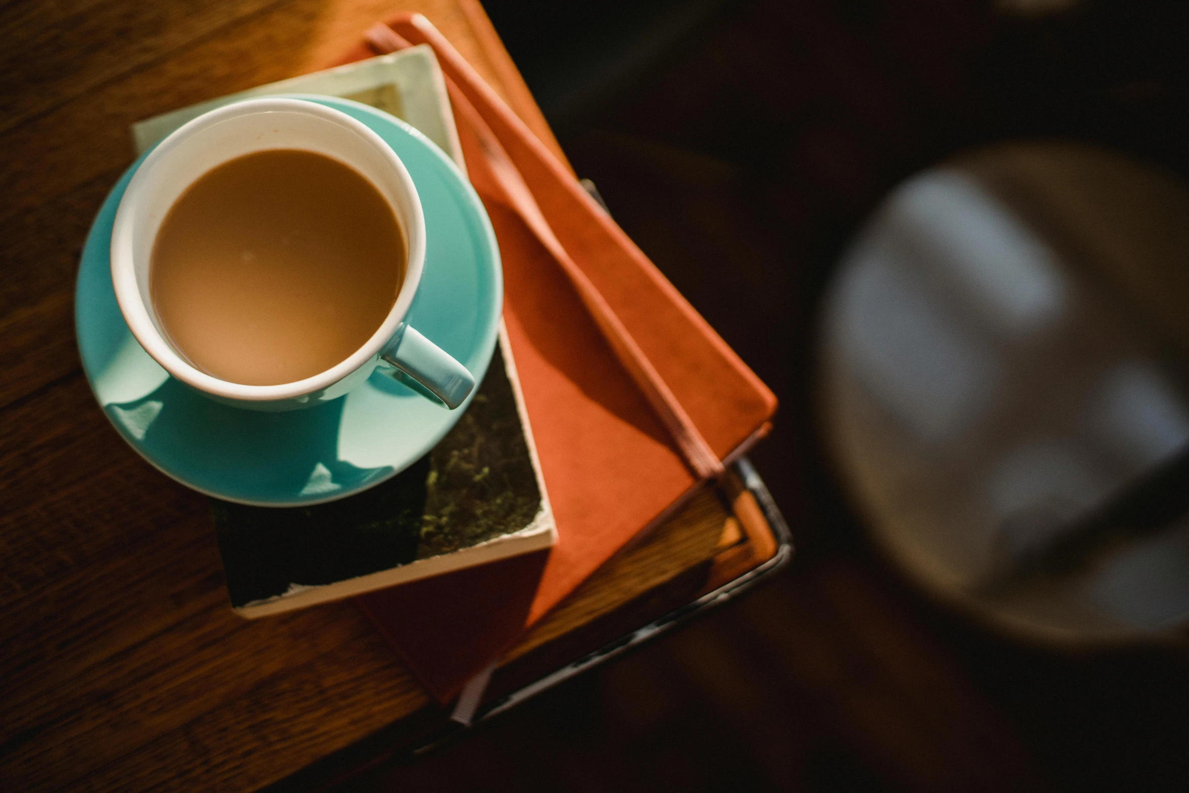 a cup of tea sitting on top of a stack of books, by Romain brook, trending on unsplash, sitting on a mocha-colored table, orange and teal color, high angle close up shot, 15081959 21121991 01012000 4k