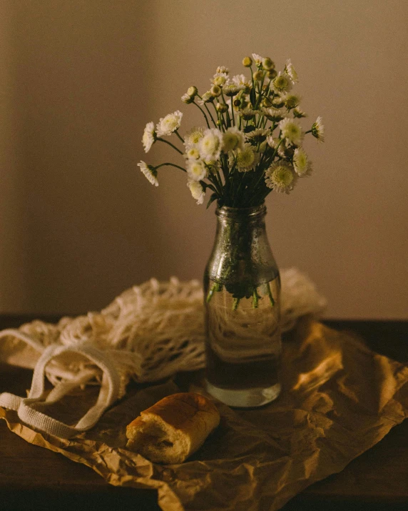 a vase filled with white flowers sitting on top of a table, a still life, unsplash, bread, ribbon, bottle, vintage photo