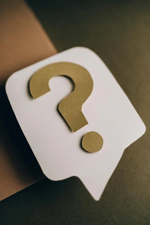 a piece of paper with a question mark on it, by Matt Cavotta, trending on pexels, modernism, brown, the riddler, white and gold color scheme, made of cardboard