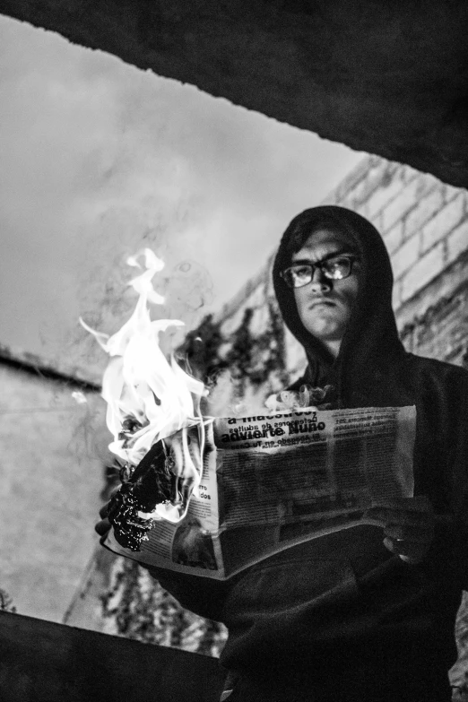 a black and white photo of a man holding a fire, a black and white photo, inspired by David Wojnarowicz, pexels contest winner, surrealism, man with glasses, newspaper photograph, in a hood, superhero