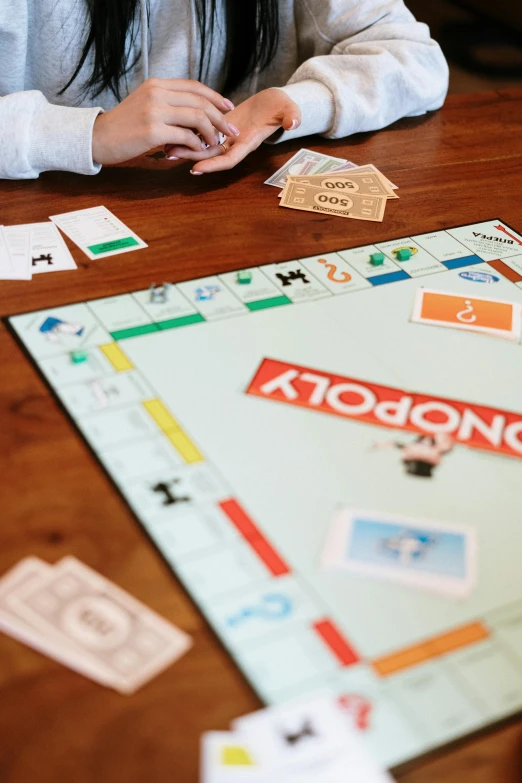 a woman sitting at a table playing monopoly, on a wooden table, uncrop, thumbnail, sydney