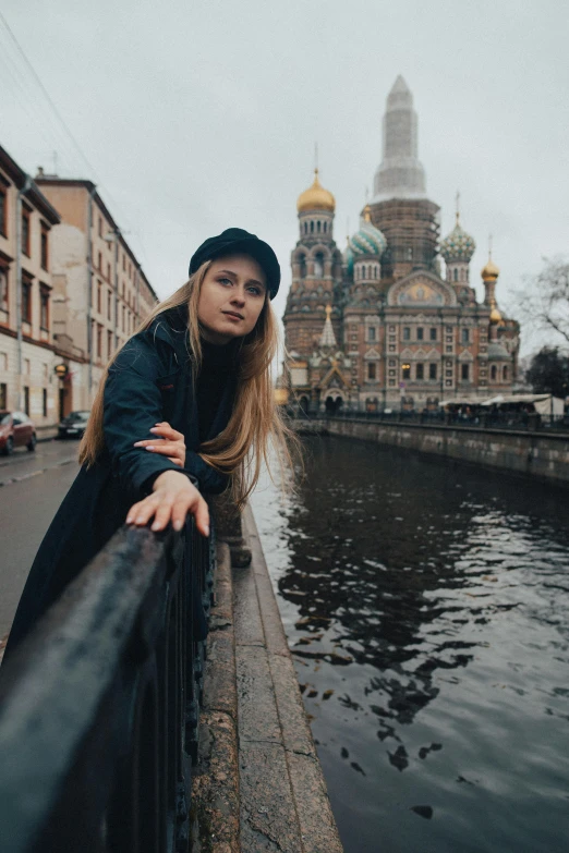 a woman leaning on a railing next to a body of water, pexels contest winner, renaissance, russian city, with black beanie on head, square, a blond