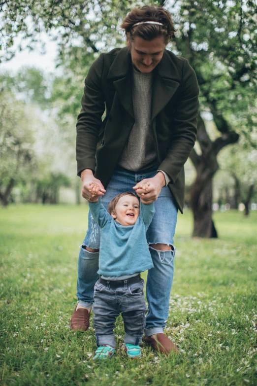 a man holding the hands of a small child, pexels contest winner, standing on two legs, in a park, baggy jeans, looking happy