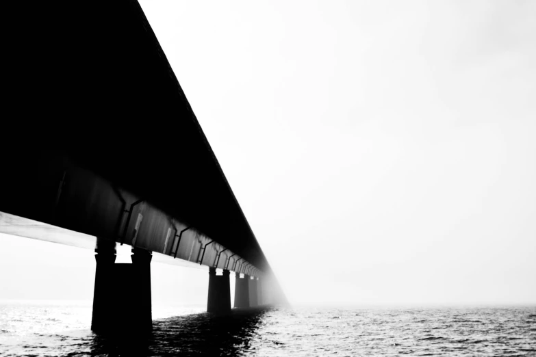 a black and white photo of a bridge over a body of water, a black and white photo, by Karl Buesgen, unsplash, minimalism, white fog painting, 1024x1024, sea underneath, highway