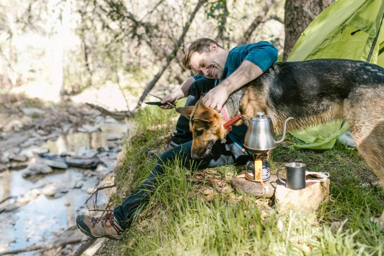 a man sitting next to a dog in front of a tent, unsplash, peacefully drinking river water, avatar image, full frame image, wearing adventuring gear