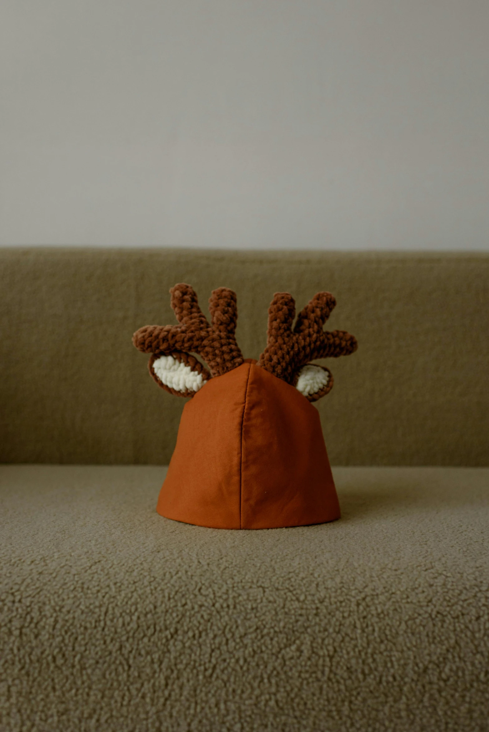 a close up of a stuffed animal on a couch, by Simon Gaon, unsplash, photorealism, horns on head, orange balaclava, in claymation, jeongseok lee