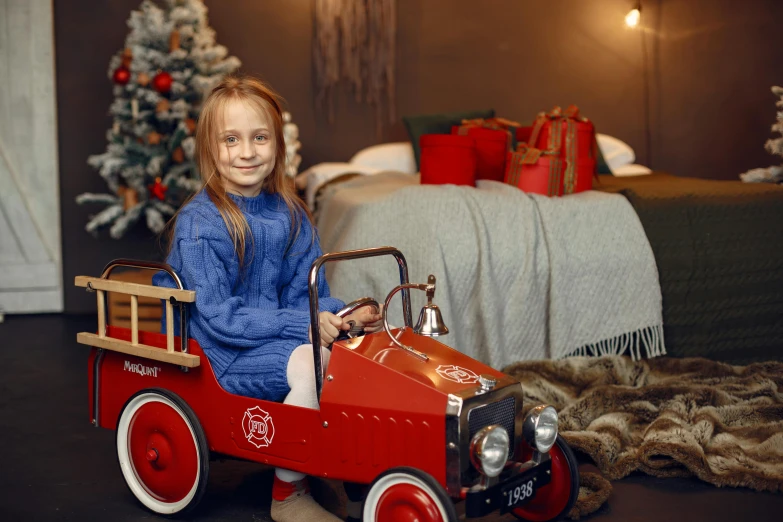 a little girl is sitting in a toy firetruck, by Julia Pishtar, pexels contest winner, fine art, sports car in the room, 8 к, christmas, vintage car