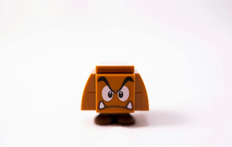 a close up of a toy on a white surface, inspired by Mario Comensoli, unsplash, angry face, square face, brown, mini figure