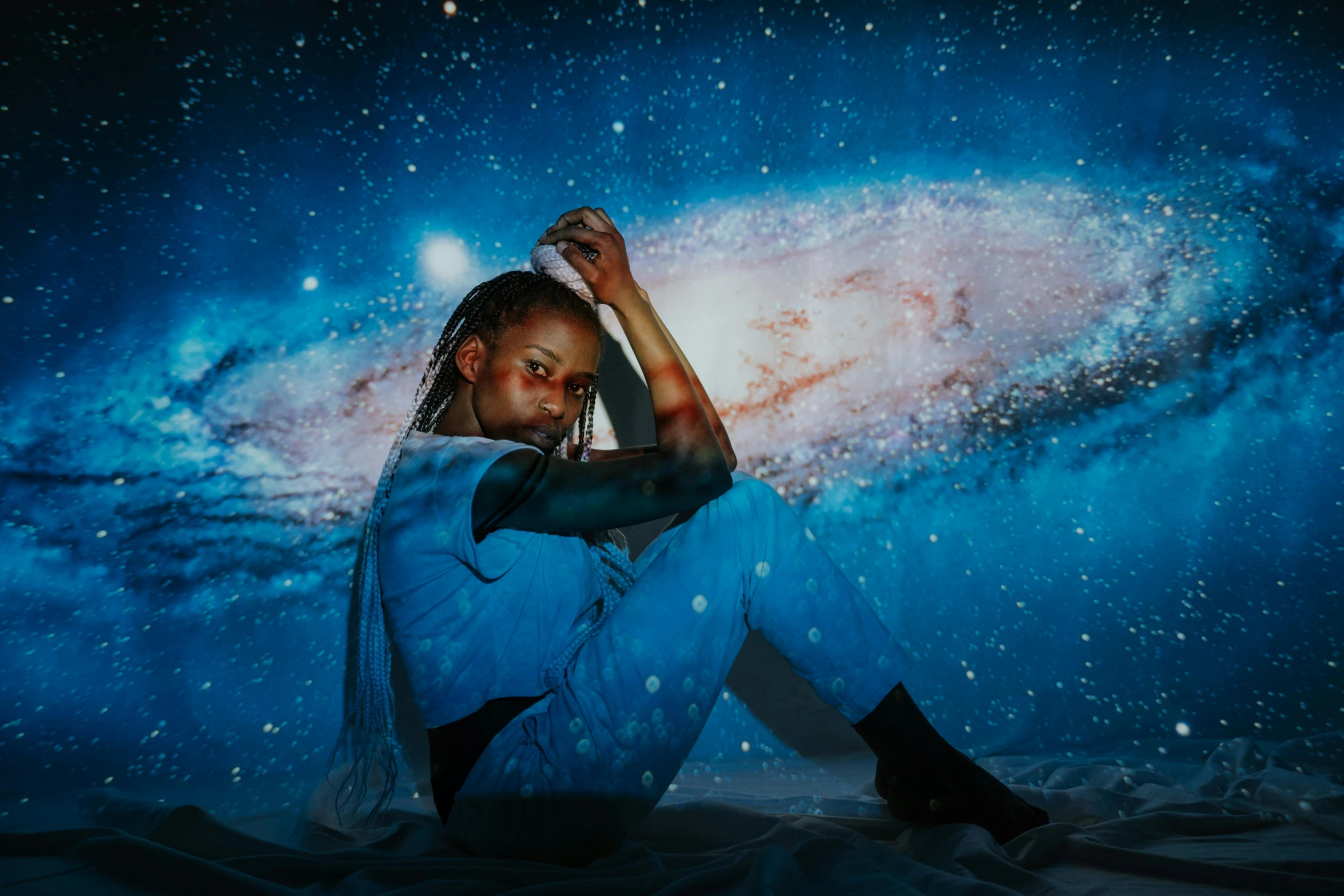 a woman sitting on the ground in front of a galaxy, an album cover, trending on pexels, afrofuturism, playboi carti portrait, standing in outer space, galaxy themed room, transparent celestial light gels