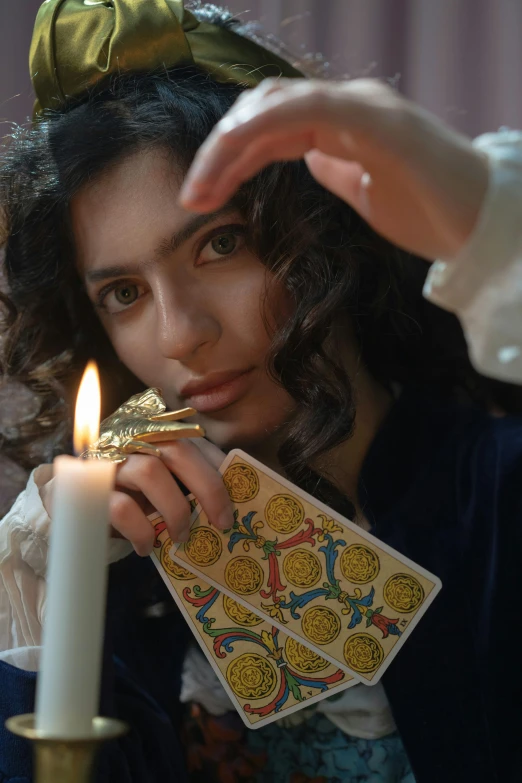 a woman holding a deck of cards next to a candle, trending on pexels, qajar art, looking towards camera, a young female wizard, profile image, young middle eastern woman