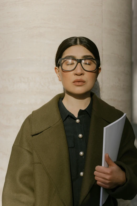 a woman in glasses holding a piece of paper, an album cover, inspired by Ruth Jên, trending on pexels, unibrow, wearing jacket, holding a giant book, portrait androgynous girl