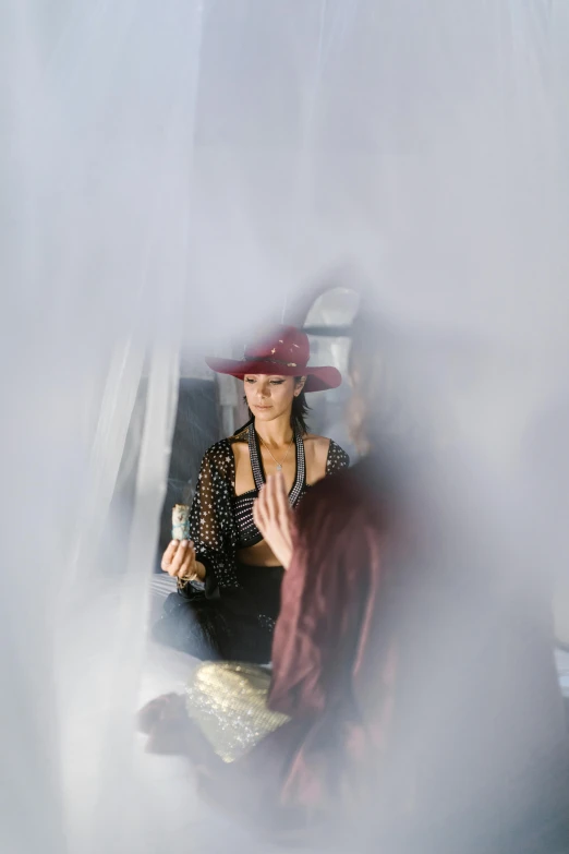 a woman in a red hat sitting in a chair, a picture, unsplash, renaissance, dry ice, fashion week backstage, transparent veil, a high angle shot