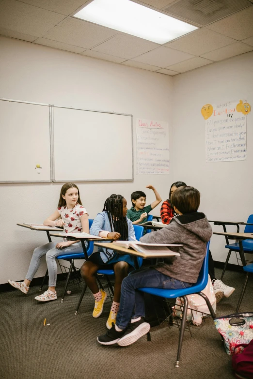 a group of children sitting at desks in a classroom, by Everett Warner, trending on unsplash, fan favorite, calmly conversing 8k, low quality photo, thumbnail