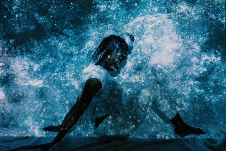 a woman sitting on top of a bed under water, by Lucia Peka, pexels contest winner, light and space, blue particles, photo of a black woman, water is made of stardust, teamlab