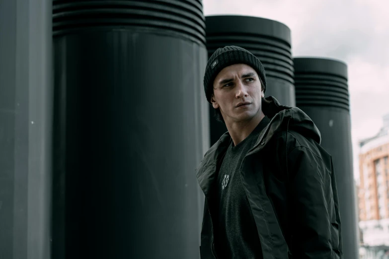 a man standing in front of a row of black poles, a portrait, inspired by Anthony Devas, pexels contest winner, model wears a puffer jacket, chappie in an adidas track suit, parkour, f 1 driver charles leclerc