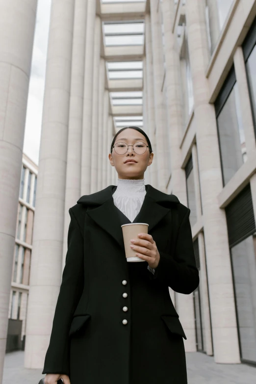 a woman in a black coat holding a cup of coffee, inspired by Fei Danxu, trending on unsplash, renaissance, tall thin build, in strict suit, walking towards the camera, high collar