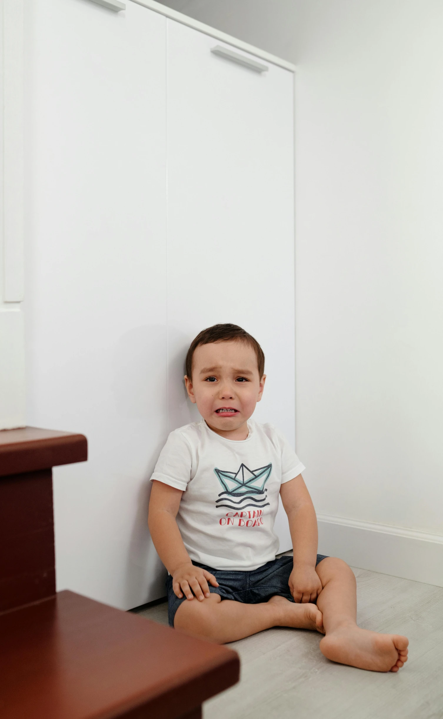 a little boy that is sitting on the floor, wearing a marijuana t - shirt, sitting on the porcelain throne, crying, in a white room