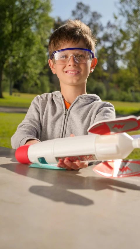 a young boy sitting at a table with a model airplane, holding a rocket, avatar image, angled shot, multi-part