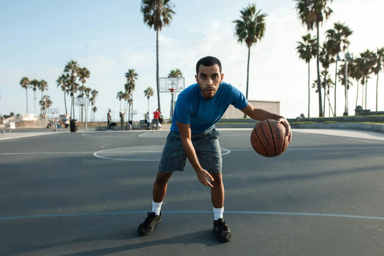 a man standing on a basketball court holding a basketball, by Dan Luvisi, dribble, long beach background, facing camera, mohamed chahin, profile image