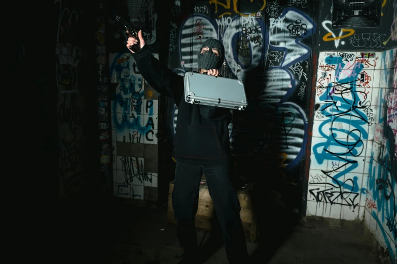 a man holding a briefcase in front of a graffiti covered wall, inspired by Banksy, unsplash, graffiti, action poses with weapons, underground party, background image