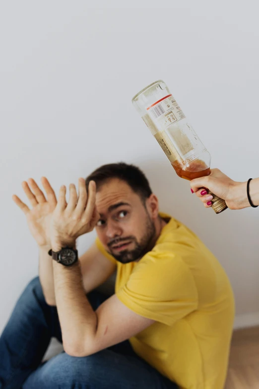 a man sitting on the floor next to a woman holding a bottle of alcohol, a cartoon, trending on pexels, renaissance, holding his hands up to his face, man standing in defensive pose, headshot photo, disappointed