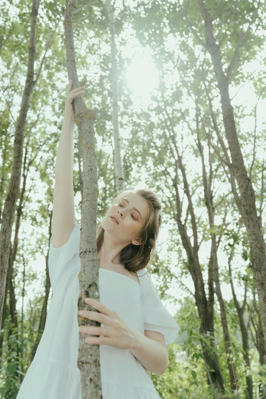 a woman standing next to a tree in a forest, an album cover, unsplash, medium format. soft light, color footage, ignant, white wood