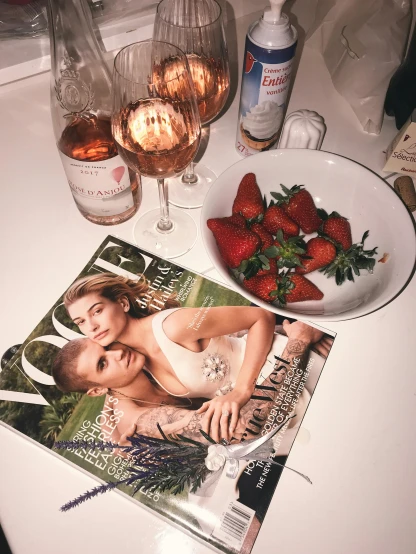 a magazine sitting on top of a table next to a bowl of strawberries, a picture, vogue photo, 🎀 🧟 🍓 🧚, drinking wine, late night