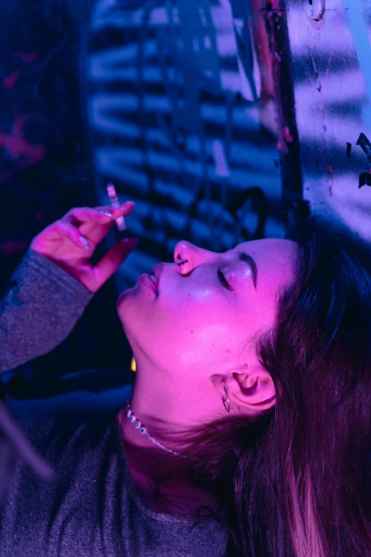 a woman smoking a cigarette in a dark room, inspired by Elsa Bleda, trending on pexels, visual art, purple and pink and blue neons, laying down, at a rave, movie still of a tired