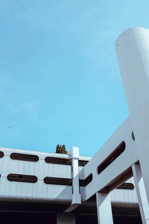 a tall white building sitting under a blue sky, inspired by Ricardo Bofill, unsplash, brutalism, instagram story, parking lot, low quality photo, rooftop