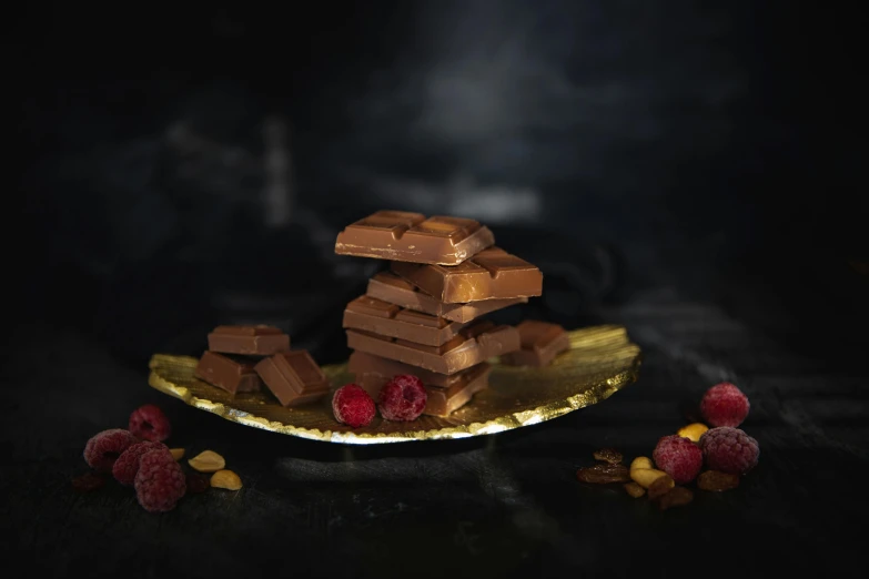 a plate topped with pieces of chocolate and raspberries, a still life, inspired by Jules Robert Auguste, pexels contest winner, product display photograph, stacked, award winning dark, made of polished broze