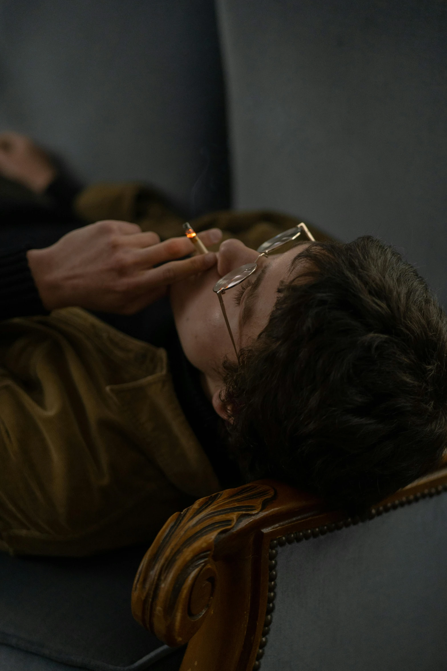 a man laying on a couch with a cigarette in his mouth, trending on pexels, serial art, timothee chalamet, andrei tarkovsky scene, wearing gold glasses, profile image