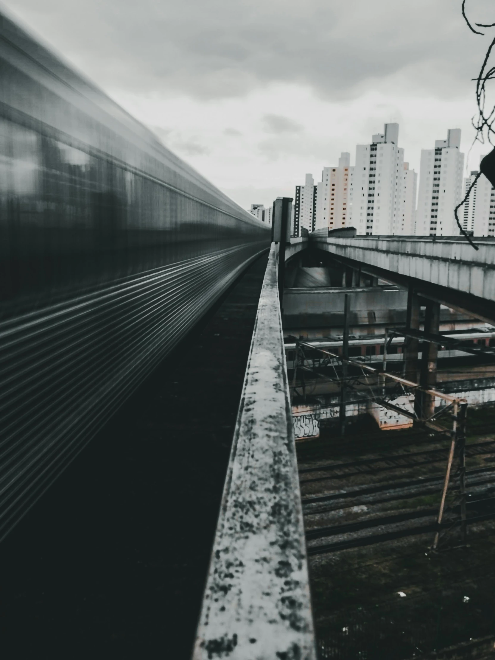 a train traveling through a city next to tall buildings, by Joze Ciuha, pexels contest winner, dreary, sky bridge, instagram story, buildings covered in black tar