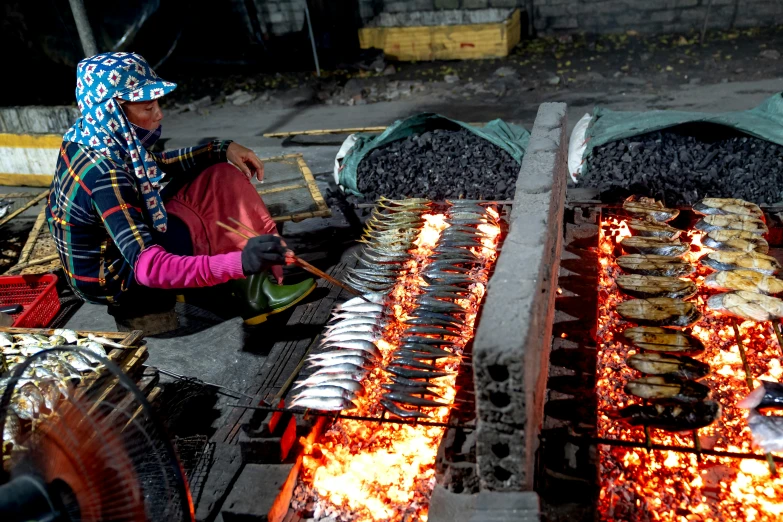a woman is cooking fish on a grill, by Gwen Barnard, pexels contest winner, process art, steel mill, sichuan, made of lava, thumbnail