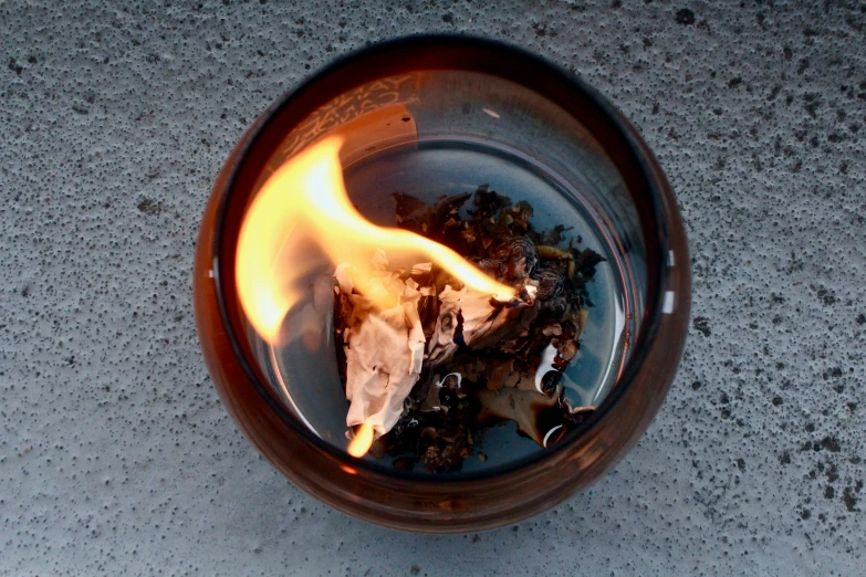 a close up of a lit candle on a table, firing it into a building, with an ashtray on top, flaming leaves, viewed from above