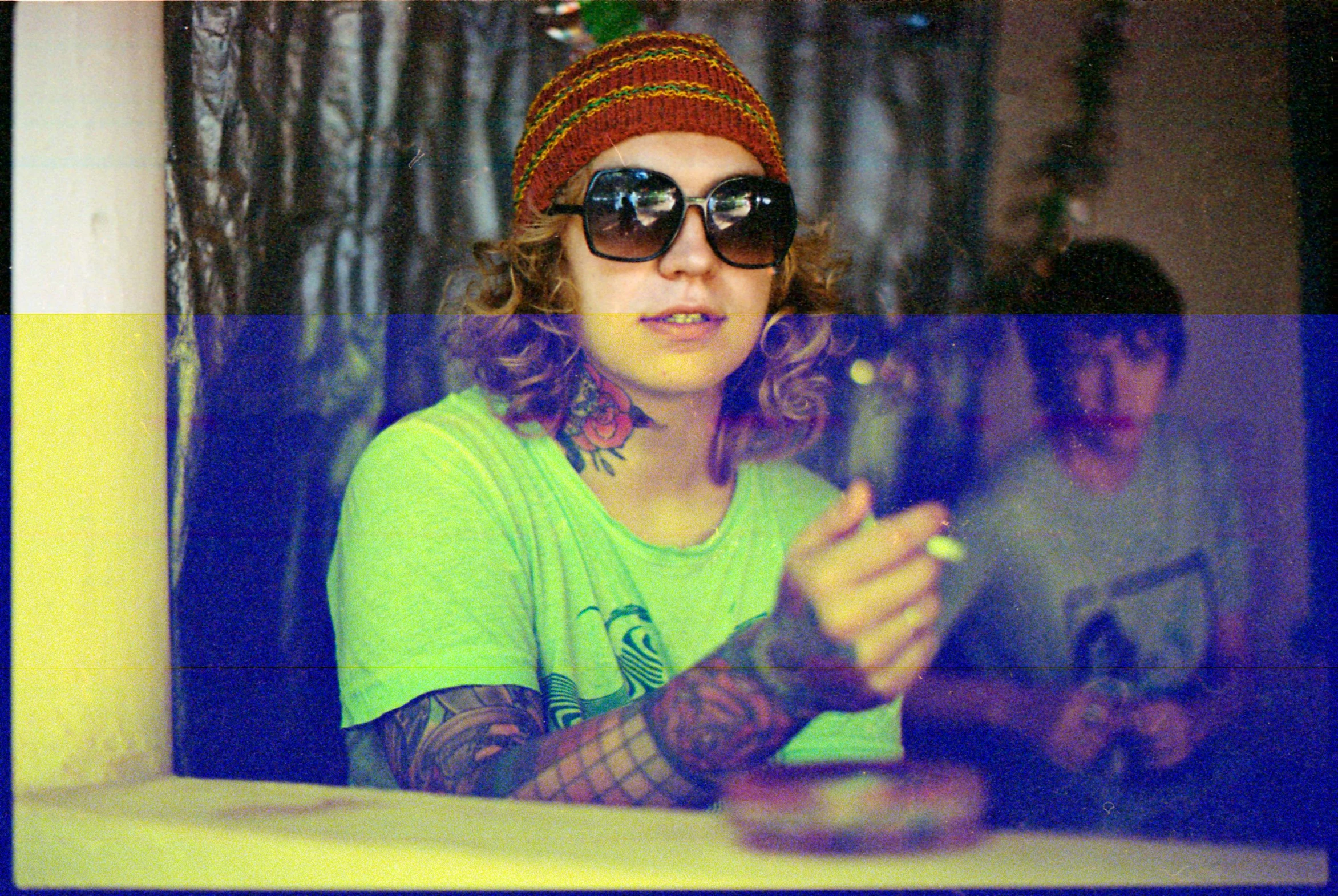 a person sitting at a table with a cell phone, an album cover, inspired by Lasar Segall, flickr, wearing sunglasses and a hat, tattoo parlor photo, scanned in, lizard king / queen forgiveing