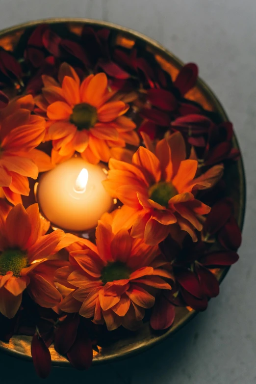 a lit candle surrounded by flowers in a bowl, orange halo, vibrant hues, lit from above, harvest