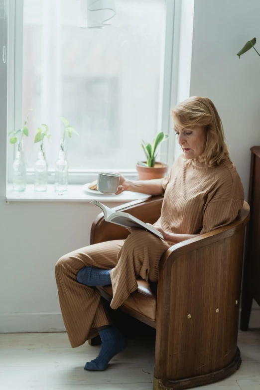 a woman sitting in a chair reading a book, wearing pajamas, muted browns, healthcare, julia hetta