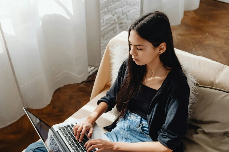 a woman sitting on a couch using a laptop, trending on pexels, asian girl with long hair, wearing a dark shirt and jeans, performing, modest