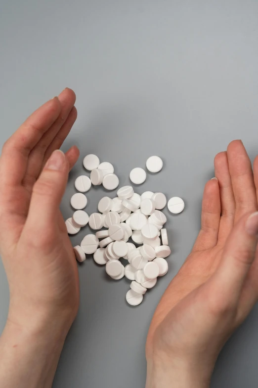 a person holding a handful of pills in their hands, by Adam Marczyński, plasticien, on a white table, ap, round-cropped, 8l