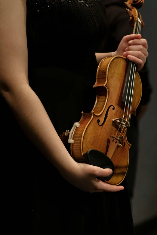 a woman in a black dress holding a violin, holding a wood piece, photographed for reuters, right hand side profile, promo image