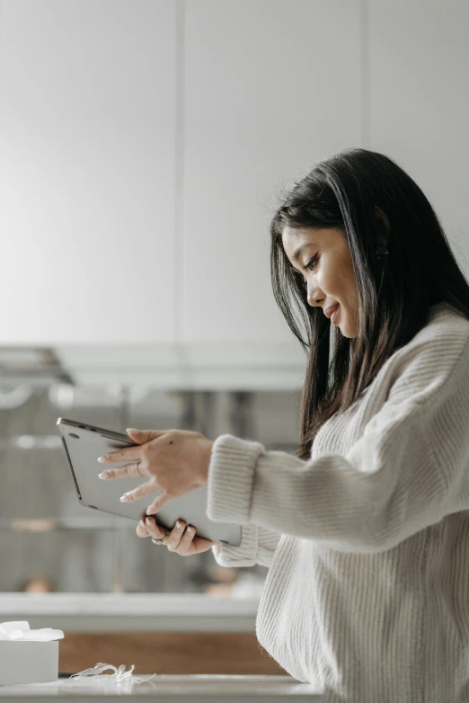 a woman standing in a kitchen looking at her cell phone, trending on pexels, asian girl with long hair, using a magical tablet, white sweater, gif