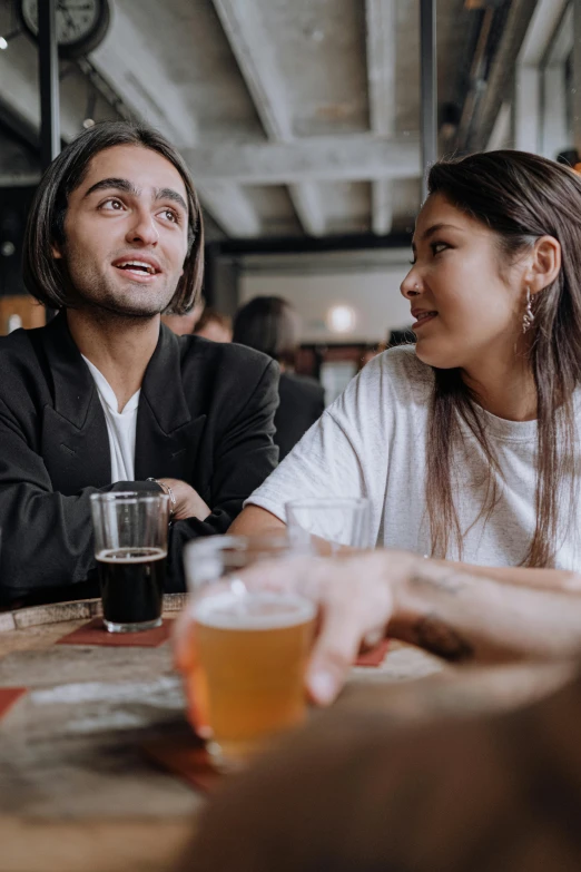 a man and a woman sitting at a table with beers, pexels contest winner, flirting expression, a man wearing a black jacket, tyler edlin and natasha tan, customers