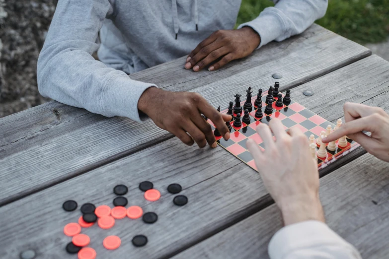 two people playing a game of checkers on a picnic table, by Carey Morris, pexels contest winner, dark grey and orange colours, multiplayer set-piece :9, closeup of arms, payne's grey and venetian red