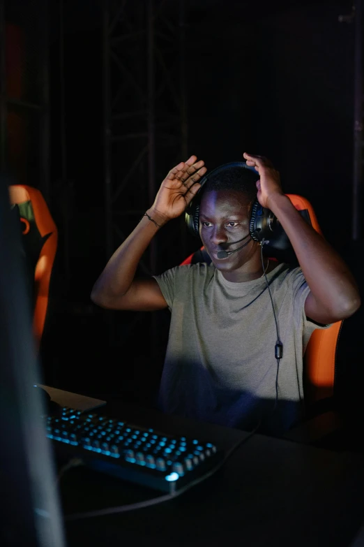 a man wearing headphones sitting in front of a computer, afrofuturism, esports, very kenyan, holding his hands up to his face, photograph taken in 2 0 2 0