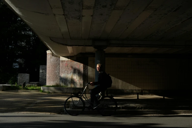 a man riding a bike under a bridge, by Tobias Stimmer, strong shadows), resting, portait image