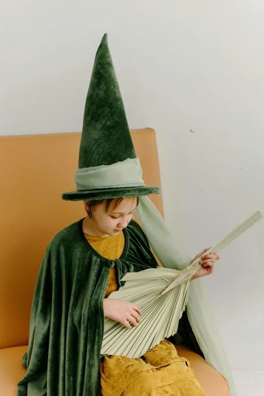 a little boy dressed as a wizard reading a book, an album cover, inspired by Kate Greenaway, pexels, renaissance, green corduroy pants, extra large witch hat, indoor picture, costume design made with love